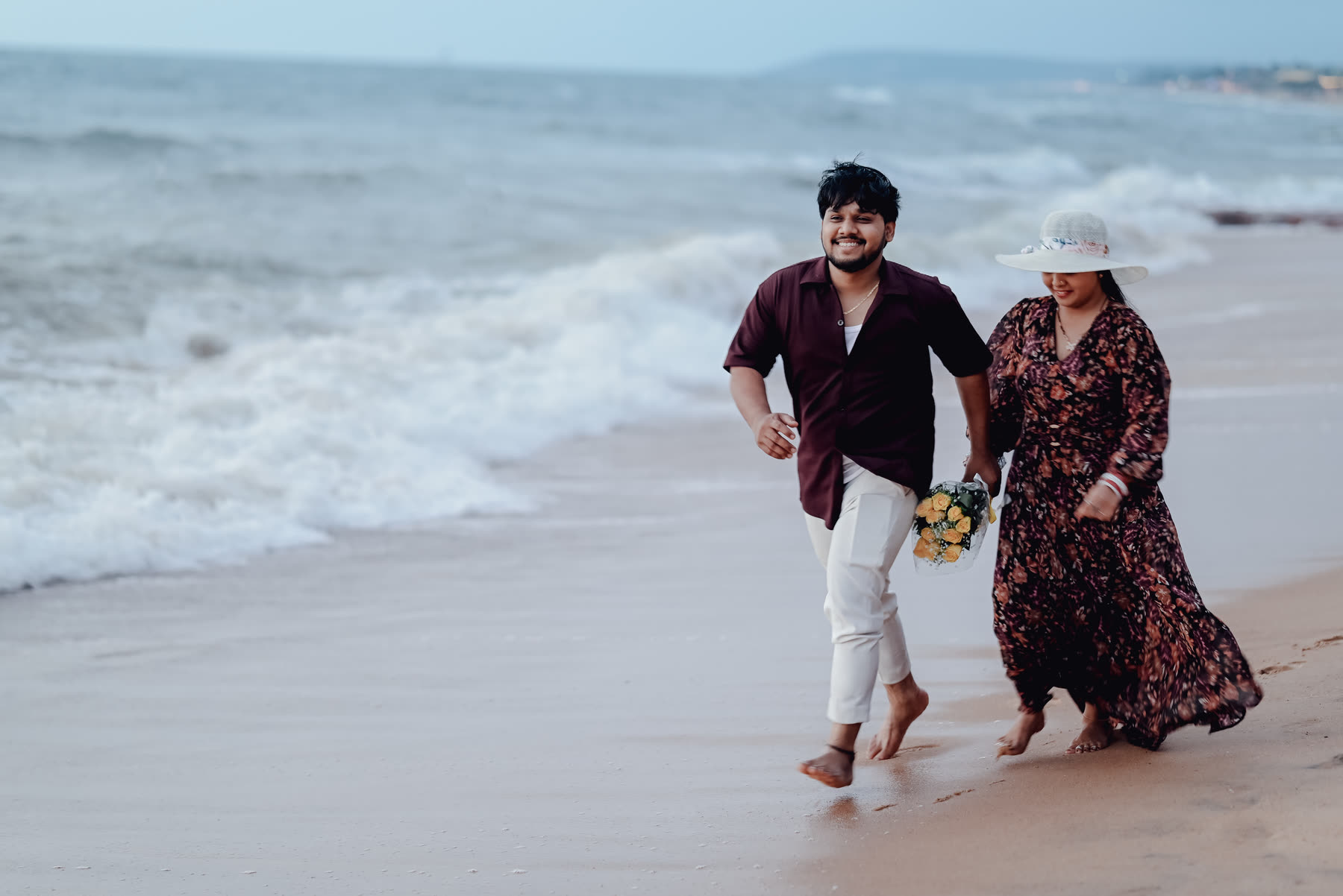 Couple walking the shoreline at dusk, bouquet in hand
