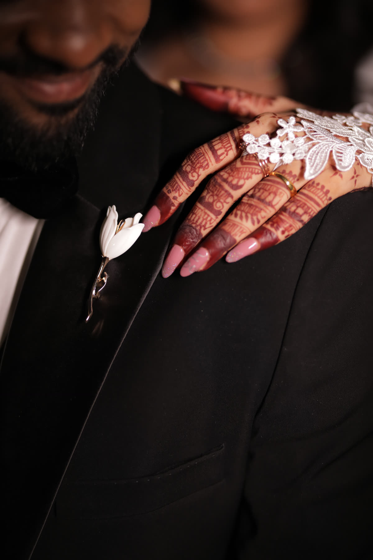 A mehendi hand on a black lapel and boutonniere