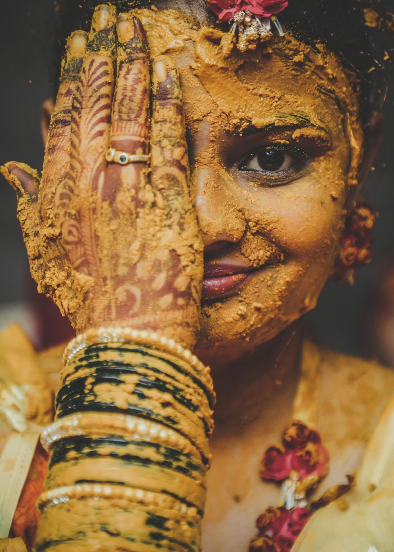 Turmeric-covered, one mehendi hand across her face